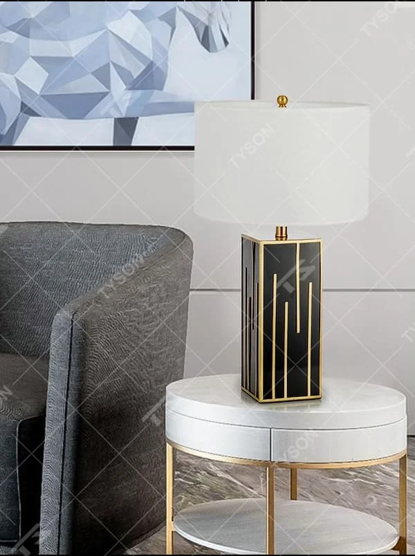 This is a luxury geometric - shaped table lamp with a black - gold geometric base (decorated with gold lines) and a white cylindrical fabric lampshade, featuring a minimalist luxury design with strong modern artistic sense. It is used for local desktop lighting and decoration, creating a luxurious and elegant atmosphere. It is suitable for luxury - style home bedroom bedside tables, high - end hotel guest rooms, modern soft decoration display spaces and other places.