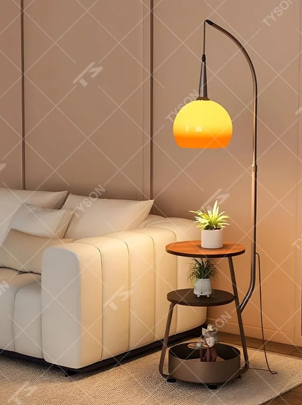 This is a modern multi-functional floor lamp with a curved metal pole, a gradient orange-yellow spherical lampshade, and integrated multi-layer storage shelves, featuring a minimalist and practical design. It is used for space lighting, storage, and decoration, creating a warm and practical atmosphere. It is suitable for modern home living rooms, small-sized residences, creative studios and other places.