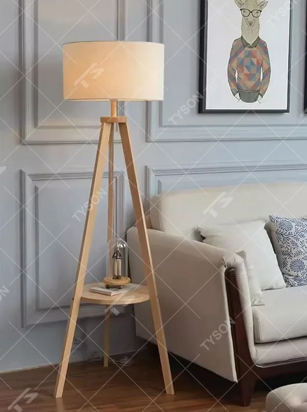 This is a Nordic-style wooden tripod floor lamp, with a light wood tripod stand (with a circular storage table) and a beige fabric cylindrical lampshade, featuring a minimalist and natural design with a warm ambiance. It is used for space lighting and storage decoration, creating a warm and natural atmosphere. It is suitable for Nordic-style home living rooms, minimalist residences, leisure reading areas and other places.