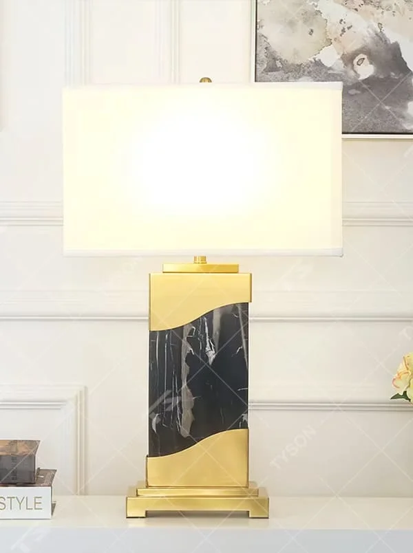 This is a luxury black-gold marble table lamp, with a golden metal frame, black-veined marble (with curved design), and a white fabric square lampshade, featuring a minimalist luxury design with high-quality texture. It is used for local desktop lighting and decoration, creating a high-end luxury atmosphere. It is suitable for luxury-style home bedroom bedside tables, high-end hotel guest rooms, modern soft decoration display spaces and other places.