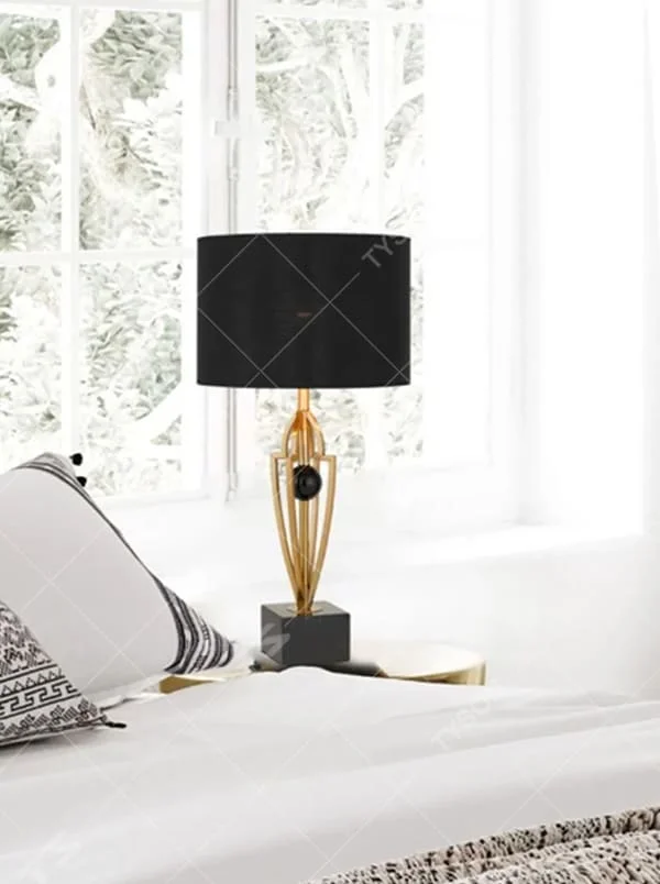 This is a luxurious retro-style table lamp with a golden metal bracket, a black square base, and a black fabric lampshade. It features a grand and elegant design with artistic texture. It is used for local desktop lighting and decoration, creating a luxurious retro ambiance. It is suitable for luxury-style home bedrooms, high-end hotel guest rooms, art exhibition halls and other places.