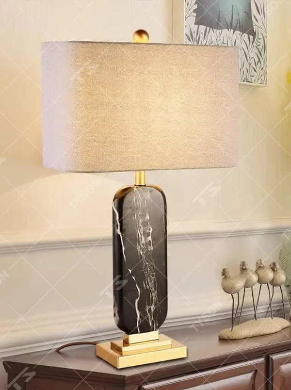 This is a luxury black-gold marble table lamp, with a black-veined marble base, golden metal components, and a gray fabric square lampshade, featuring a minimalist luxury design with high-quality texture. It is used for local desktop lighting and decoration, creating a high-end luxury atmosphere. It is suitable for luxury-style home bedroom bedside tables, high-end hotel guest rooms, modern soft decoration display spaces and other places.