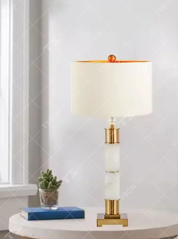 This is a luxury-style gold and white table lamp, combining golden metal and white cylinder, with a beige fabric circular lampshade, featuring a minimalist and grand design with strong luxury texture. It is used for local desktop lighting and decoration, creating a luxury and warm atmosphere. It is suitable for luxury-style home bedroom bedside tables, high-end hotel guest rooms, modern minimalist living room side tables and other places.