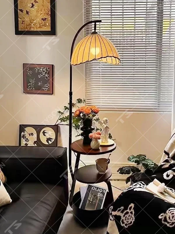 This is a modern multi-functional arc floor lamp with a black metal arc pole, a shell-shaped fabric lampshade, and integrated multi-layer storage shelves, featuring a minimalist and practical design. It is used for space lighting, storage, and decoration, creating a warm and practical atmosphere. It is suitable for modern home living rooms, small-sized residences, leisure reading areas and other places.