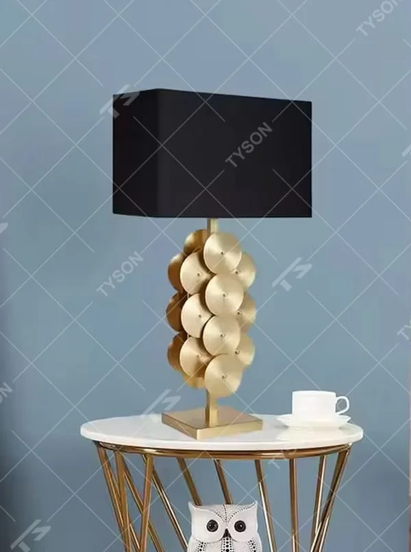 This is a luxury-style black and gold table lamp, with a golden disc-stacked base and a black square fabric lampshade, featuring a minimalist and grand design with strong luxury texture. It is used for local desktop lighting and decoration, creating a luxury and modern atmosphere. It is suitable for luxury-style home bedroom bedside tables, high-end hotel guest rooms, modern minimalist living room side tables and other places.