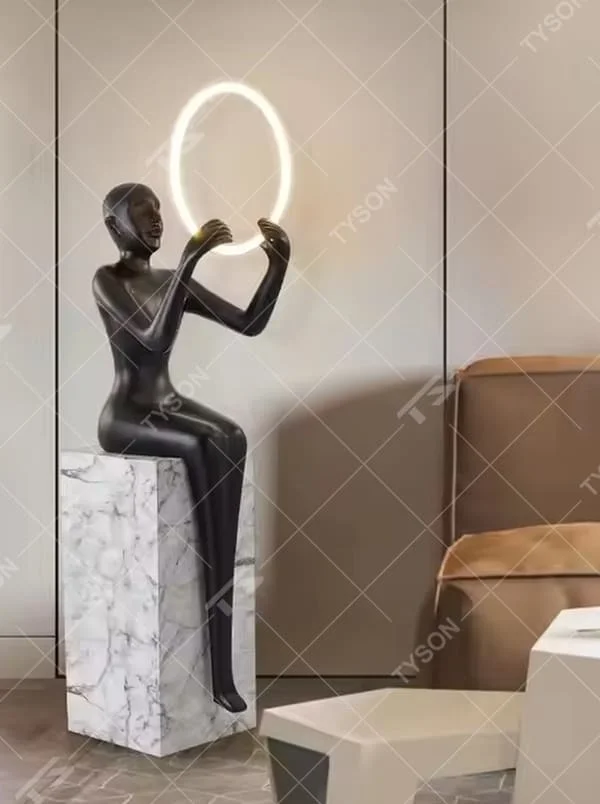 This is an artistic human-shaped floor lamp, featuring a black human sculpture holding a circular luminous lamp, with a white marble base. It has a strong artistic sense and modern luxury style. It is used for space lighting and decoration, creating an artistic atmosphere. It is suitable for modern art home living rooms, high-end hotel lobbies, art exhibition halls and other places.
