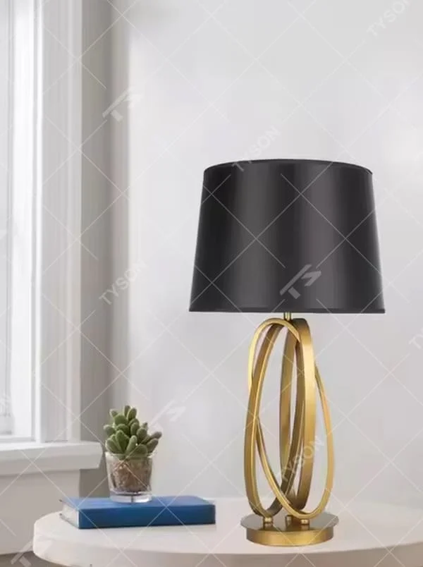 This is a modern luxury circular metal table lamp, with a golden interlaced circular metal base and a black fabric conical lampshade, featuring an artistic design and strong luxury texture. It is used for local desktop lighting and decoration, creating a high-end luxury atmosphere. It is suitable for luxury-style home bedroom bedside tables, modern minimalist living room side tables, high-end hotel guest rooms and other places.