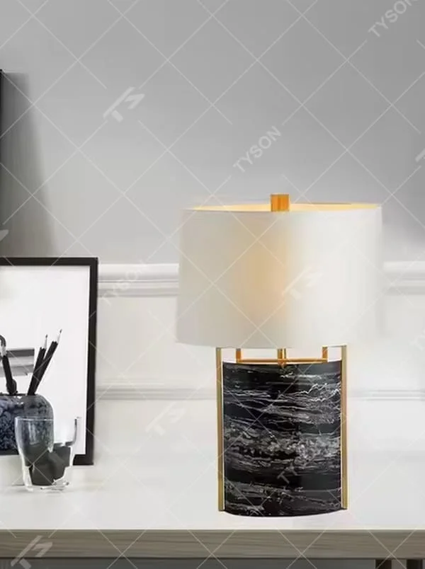 This is a luxury marble table lamp, with a black-veined marble base, a golden metal frame, and a white cylindrical fabric lampshade, featuring a minimalist luxury design with strong modern texture. It is used for local desktop lighting and decoration, creating a high-end luxury atmosphere. It is suitable for luxury-style home bedroom bedside tables, high-end hotel guest rooms, modern soft decoration display spaces and other places.