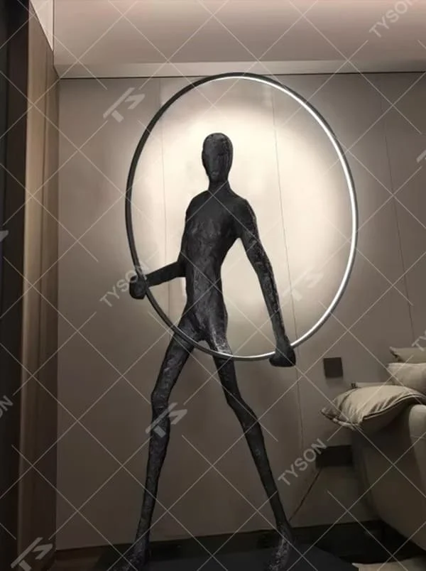 This is an artistic installation-style human sculpture ring floor lamp, featuring a black human sculpture shape paired with a circular LED light. It has a strong sense of art and avant-garde, with soft lighting and visual impact. It is used for space lighting and artistic decoration, creating a modern artistic and avant-garde atmosphere. Suitable for art exhibition halls, high-end villa living rooms, designer studios and other places.