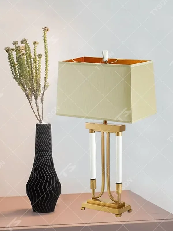 This is a retro elegant-style gold and white fabric table lamp, with a golden metal bracket (with white column elements) and a beige fabric square lampshade (orange interior). It features a retro and exquisite design, with warm and soft lighting. It is used for local desktop lighting and decoration, creating a retro and elegant atmosphere. Suitable for retro-style bedrooms, European-style living rooms, high-end homestays and other places.