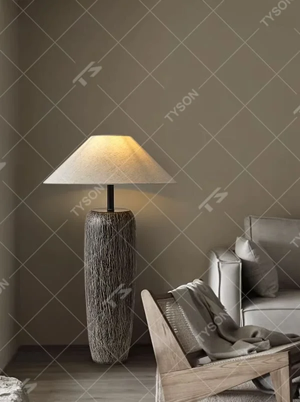 This is a natural wabi-sabi style gray textured column floor lamp, with a gray textured column base, a beige fabric conical lampshade, and a black metal pole connection. It features a minimalist and natural design with a rustic texture. It is used for space lighting and decoration, creating a warm and rustic atmosphere. Suitable for wabi-sabi style living rooms, Japanese-style bedrooms, natural-style homestays and other places.
