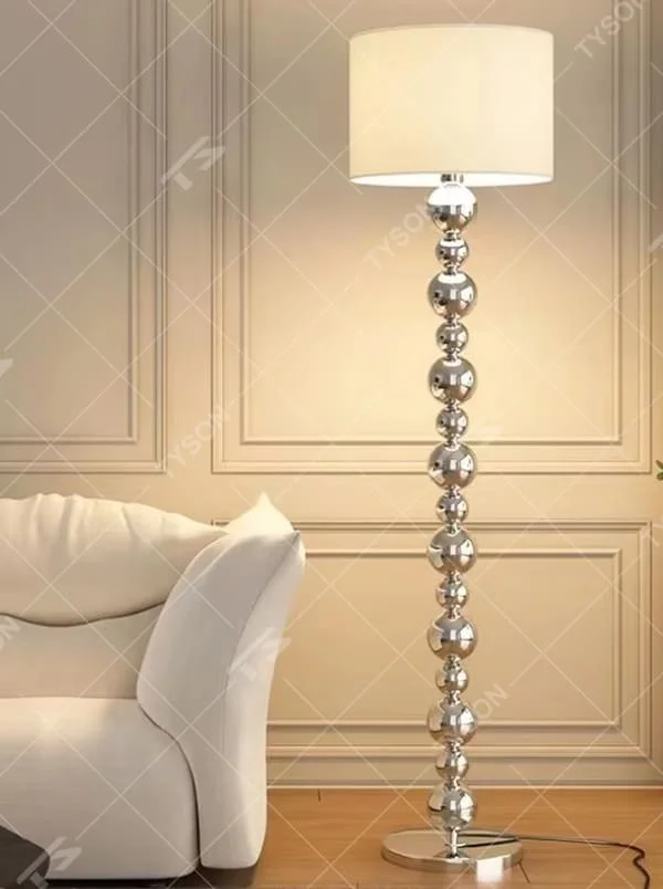 This is a light luxury exquisite silver metal ball column floor lamp, with silver metal balls layered to form a column, paired with a beige fabric round lampshade. It features a light luxury and exquisite design, with soft lighting. It is used for space ambient lighting and decoration, creating a light luxury elegant atmosphere. Suitable for light luxury-style living rooms, modern minimalist bedrooms, high-end hotel guest rooms and other places.
