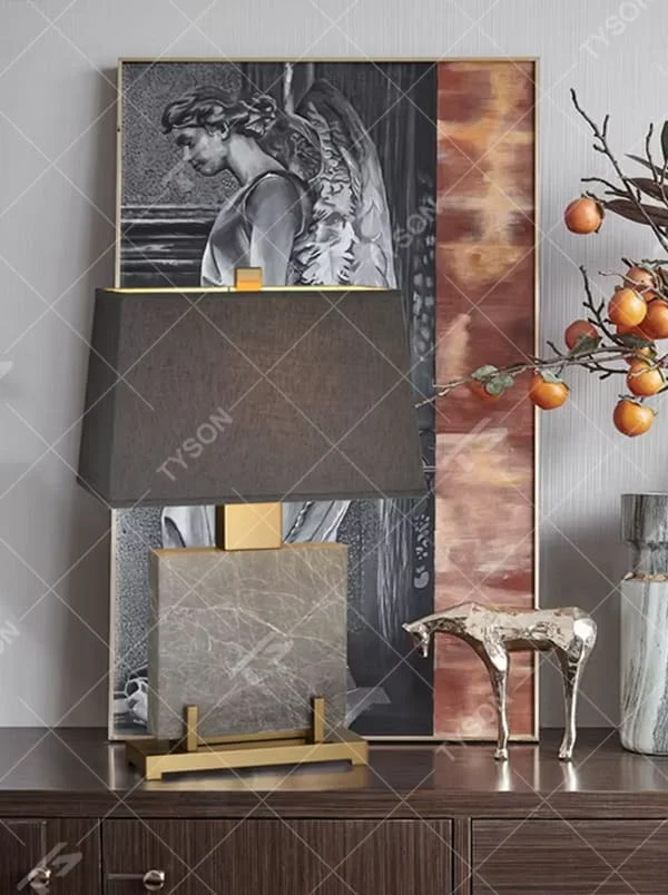 This is a light luxury modern-style marble metal fabric table lamp, with a gray marble base paired with golden metal brackets and connectors, and a gray fabric square lampshade. It features a minimalist and grand design with high texture. It is used for local desktop lighting and decoration, creating a light luxury and elegant atmosphere. Suitable for light luxury-style bedroom bedside tables, modern minimalist living room side tables, high-end hotel guest rooms and other places.