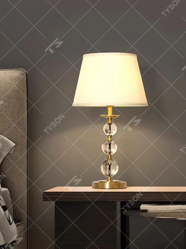 This is a light luxury exquisite crystal ball column table lamp, with a golden metal base and connectors, paired with transparent crystal ball columns and a beige fabric lampshade. It features a light luxury and exquisite design, with warm and soft lighting. It is used for local desktop lighting and decoration, creating a light luxury elegant atmosphere. Suitable for light luxury-style bedroom bedside tables, modern minimalist living room side tables, high-end hotel guest rooms and other places.