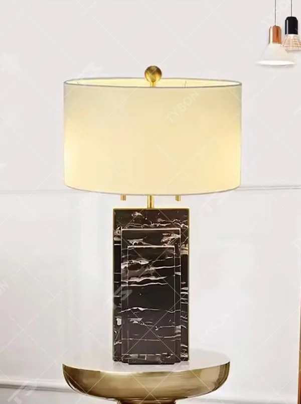 This is a luxury-style black-gold marble table lamp, with a black marble-textured base, golden metal parts, and a beige fabric circular lampshade, featuring a minimalist and grand design with strong luxury texture. It is used for local desktop lighting and decoration, creating a luxury and modern atmosphere. It is suitable for luxury-style home bedroom bedside tables, high-end hotel guest rooms, modern minimalist living room side tables and other places.