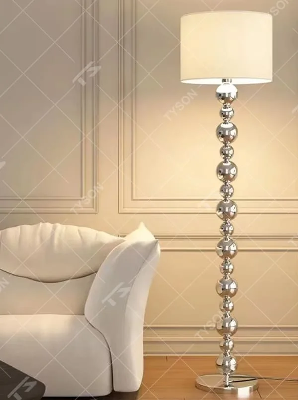 This is a modern light luxury-style silver spherical decorative floor lamp, with a silver metal pole composed of multiple spherical elements connected in series, paired with a beige fabric lampshade. It features a minimalist and textured design, with soft and warm lighting. It is used for space lighting and decoration, creating a light luxury and warm atmosphere. Suitable for modern light luxury living rooms, bedroom corners, high-end apartments and other places.