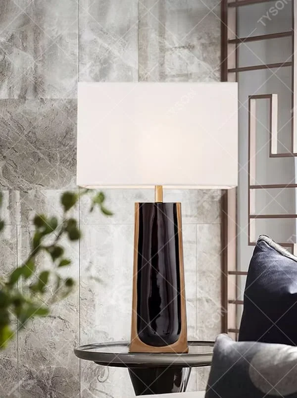 This is a light luxury modern-style black and gold column fabric table lamp, with a black and gold column base (with golden decorative edges) paired with a white fabric square lampshade. It features a minimalist light luxury design, with warm and soft lighting. It is used for local desktop lighting and decoration, creating a light luxury elegant atmosphere. Suitable for light luxury-style bedroom bedside tables, modern minimalist living room side tables, high-end hotel guest rooms and other places.