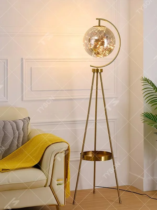 This is a light luxury modern-style golden tripod glass ball floor lamp, with a golden tripod structure, a transparent glass ball (with built-in light string) and a small tray, featuring an exquisite light luxury design, warm lighting. It is used for space lighting and decoration, creating a light luxury and warm atmosphere. Suitable for modern light luxury living rooms, bedroom corners, Nordic-style homes and other places.