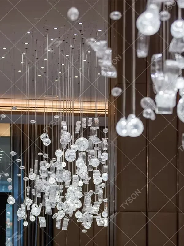 This is an artistic installation-style irregular transparent glass hanging chandelier, composed of numerous irregular transparent glass elements (spherical, block-shaped, etc.) hanging in a scattered manner by thin wires to form a three-dimensional layer. It features soft light refraction and a strong sense of modern art and spatial tension. It is used for space lighting and artistic decoration, creating a modern artistic and ethereal atmosphere. Suitable for high-end hotel lobbies, art exhibition halls, high-ceiling spaces in luxury villas and other places.