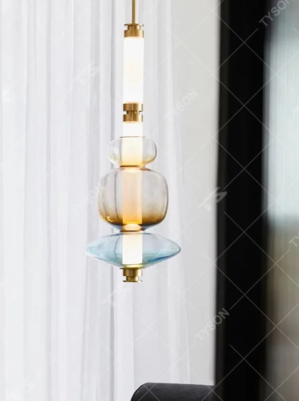 This is a modern artistic layered colorful glass chandelier, featuring a spliced shape of transparent, amber and blue glass, paired with golden metal connectors. The lighting is soft and colorful, creating an artistic and high-end atmosphere.
