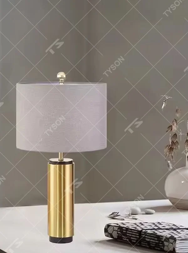 This is a light luxury minimalist golden cylinder table lamp, with a golden metal cylinder base paired with a light purple textured fabric lampshade, decorated with a small golden ball on top. The lighting is soft and warm, creating an elegant light luxury atmosphere.