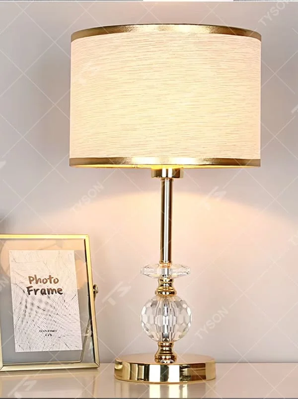 This is a light luxury exquisite fabric crystal table lamp, with a beige fabric lampshade paired with a golden trim, a golden metal lamp pole embedded with transparent cut crystal decorations, a high-quality golden base, and soft and elegant lighting, creating a light luxury exquisite atmosphere.
