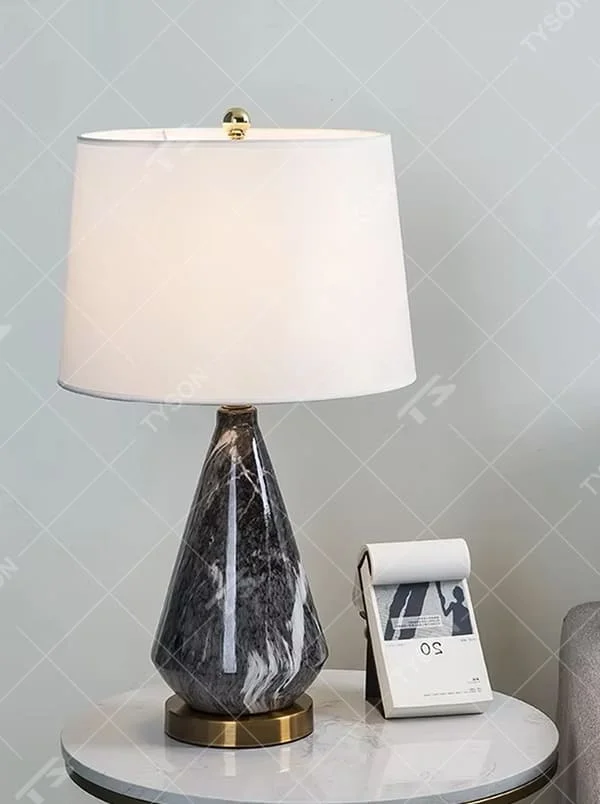 This is a light luxury marble-patterned cone table lamp, with a white fabric lampshade paired with a black-gray-white textured cone base, decorated with a golden metal base at the bottom and a small golden ball at the top. The lighting is soft and warm, creating an elegant light luxury atmosphere.