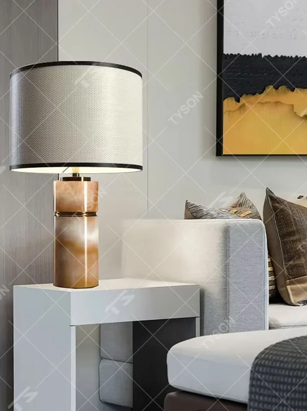 This is a light luxury minimalist table lamp, with a beige textured fabric lampshade (embellished with black trim) paired with a copper-gold layered texture base. It has an elegant and high-end style, with soft and warm lighting, creating a light luxury minimalist atmosphere.