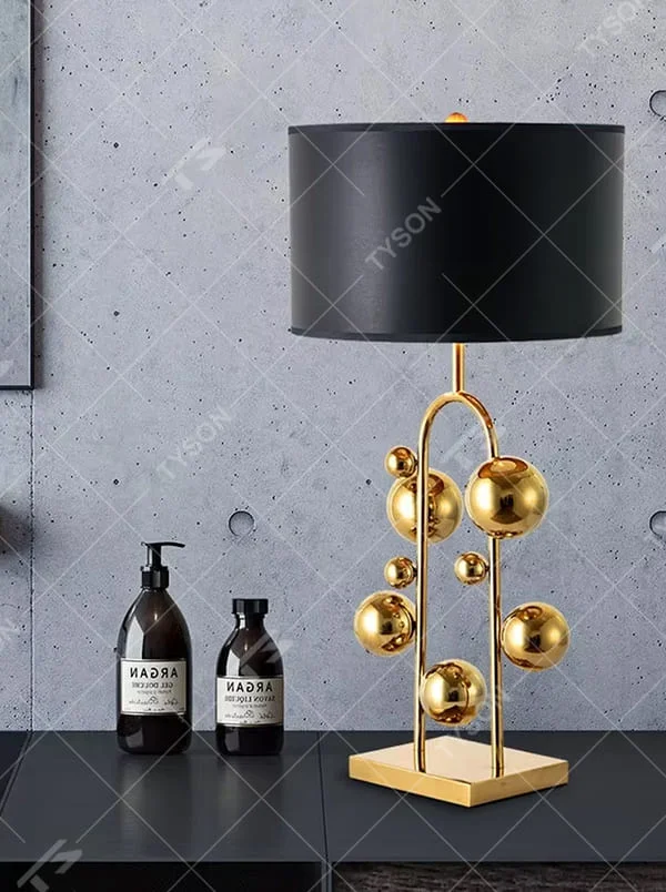 This is a light luxury modern-style golden ball table lamp, with a golden metal frame paired with multi-sized golden ball decorations, a black cylindrical lampshade + a golden square base, featuring a high-end and exquisite style, with soft and stylish lighting.