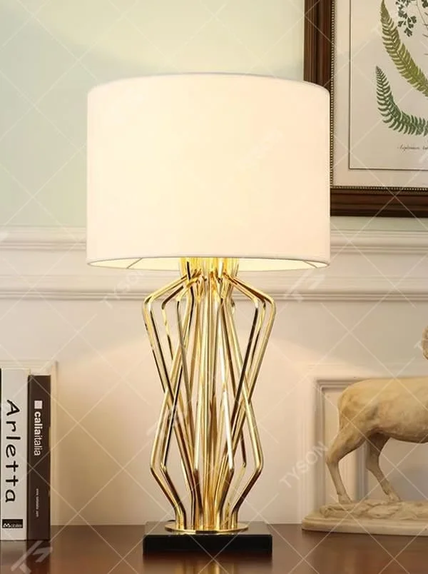 Light luxury golden interlaced hollow table lamp, white cylindrical fabric lampshade + black base, soft and warm lighting, creating a high-end elegant atmosphere.
