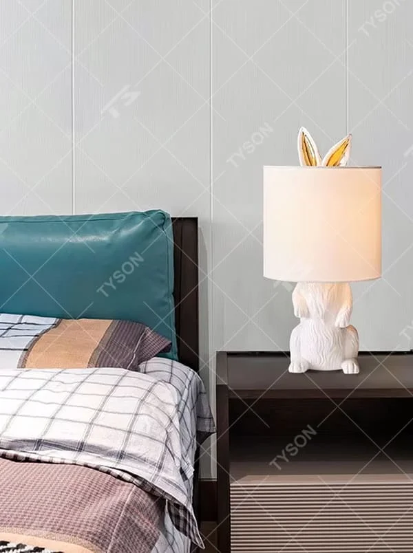 This is a cute and adorable rabbit-shaped table lamp, with a white rabbit-shaped base paired with golden ear decorations, and a white cylindrical lampshade. It has a warm and cute style, with soft and comfortable lighting.