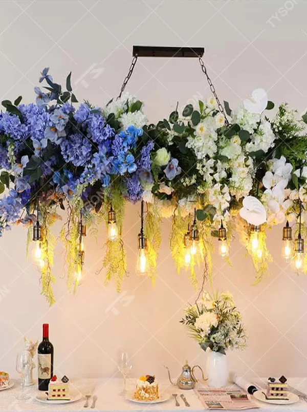 This is a romantic natural-style long strip floral retro chandelier, with blue and white artificial flowers (hydrangeas, orchids, etc.) and green plants as the main decoration, paired with retro bulbs. It has a fresh and romantic style, with warm and soft lighting.