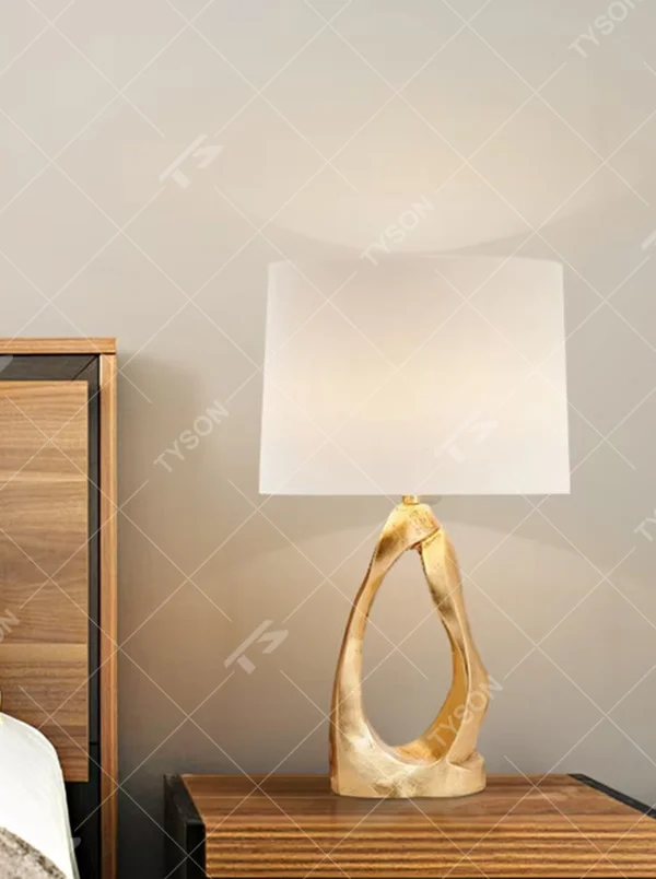 Light luxury art golden twisted hollow base table lamp, irregular metal texture base + beige fabric lampshade, soft warm light, creating a high-end artistic home atmosphere.