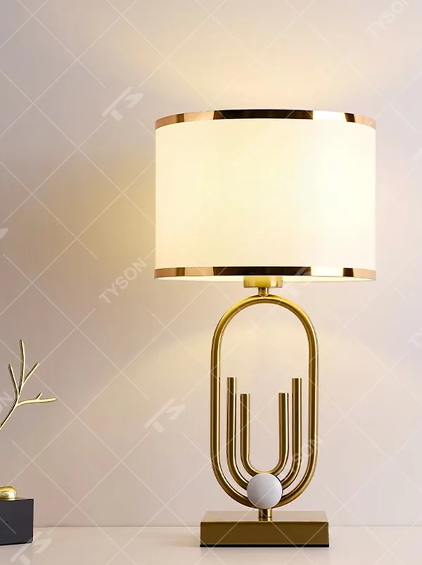Light luxury golden geometric line base table lamp, beige fabric gold-edged lampshade + golden U-shaped multi-layer frame + white small ball decoration, soft warm light, creating a modern light luxury atmosphere.