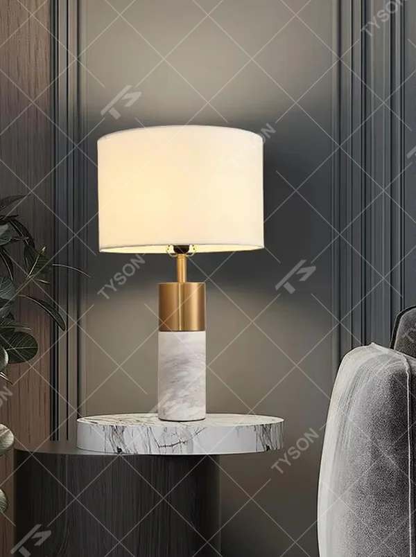 Light luxury gold-decor white marble cylindrical base table lamp, beige fabric cylindrical lampshade, soft warm light, creating a simple high-end light luxury atmosphere.