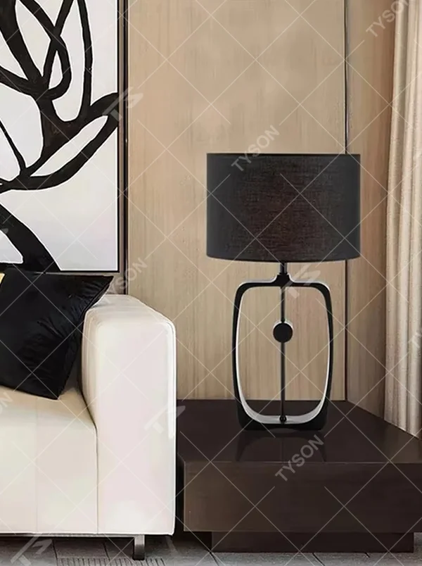 Modern minimalist black hollow frame table lamp, black fabric cylindrical lampshade + metal hollow rectangular base, soft and high-end lighting, creating a minimalist textured atmosphere.