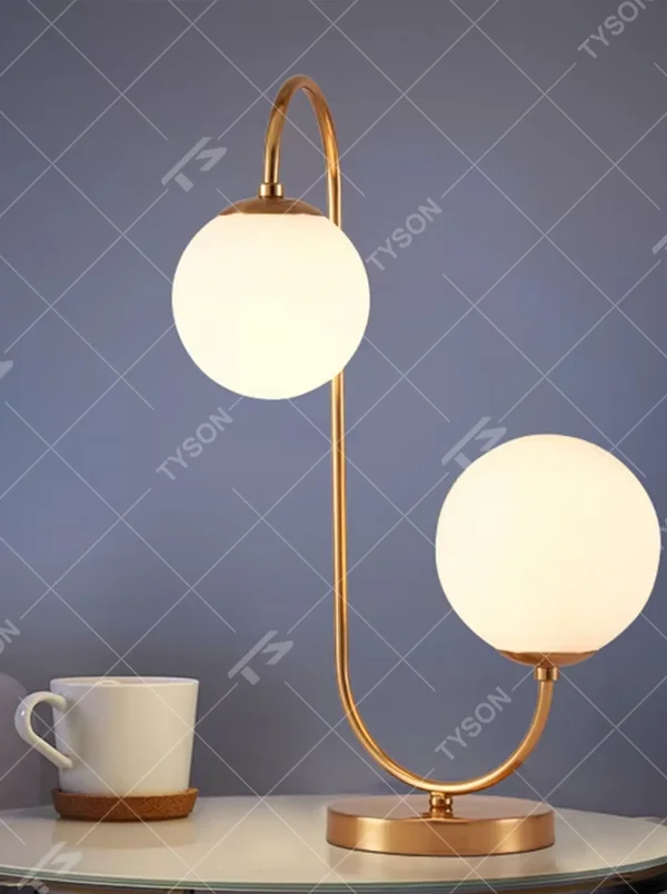 Light luxury double-ball curved table lamp (gold metal curved bracket + double milk-white glass ball lampshades + round metal base), warm light effect, creating a modern and elegant home atmosphere.
