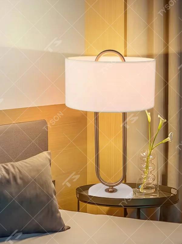 This modern light luxury table lamp features a U-shaped frame made of gold metal, paired with a white fabric rectangular lampshade and a white marble base, with a simple and elegant shape. It serves both lighting and decorative purposes, ideal for light luxury spaces such as bedroom bedside tables, living room side tables, and hotel guest rooms.