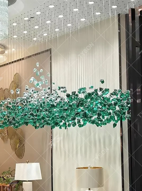 This large-scale art crystal chandelier features a long, flowing shape made of green-white gradient crystal pieces, like suspended green plants or ocean waves. It serves both lighting and artistic decorative purposes, ideal for high-ceiling commercial spaces such as hotel lobbies, sales offices, and high-end clubs.