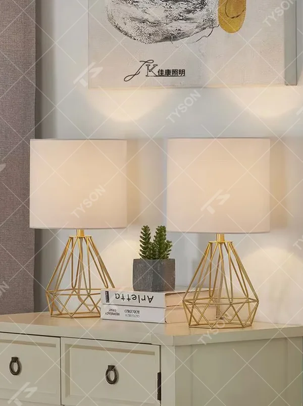 A pair of light luxury geometric iron table lamps, with gold rhombus metal frames and white fabric lampshades, providing soft and eye-protective lighting, used for lighting and decoration in home spaces, suitable for bedroom nightstands, living room side tables, hotel guest rooms, etc.