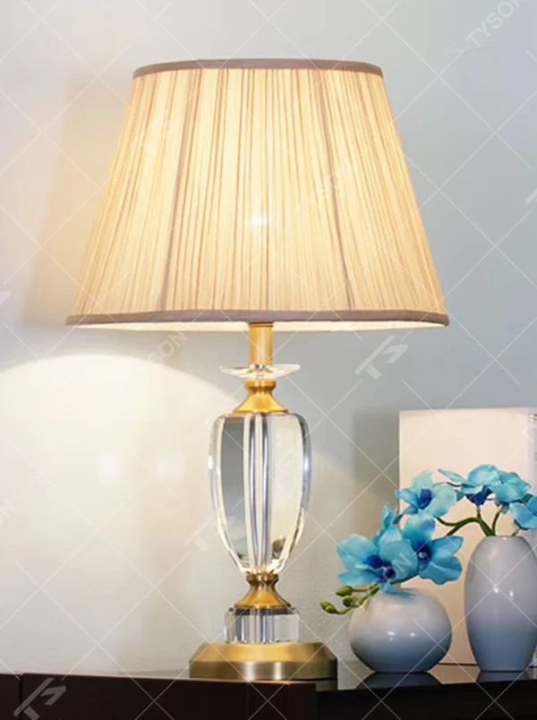 Light luxury crystal table lamp, with a transparent cut crystal column base, gold metal details and a beige pleated fabric lampshade for soft and eye-protective lighting, designed to enhance the elegant atmosphere of spaces, suitable for bedroom nightstands, living room side tables, hotel guest rooms, etc.