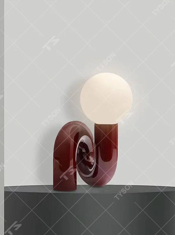 This art table lamp features a spiral S-shaped stand made of glossy wine-red material, paired with a milky white spherical lampshade, with a vivid and retro shape, serving both lighting and decorative purposes, ideal for bedrooms, living rooms, internet-famous shops and other spaces.