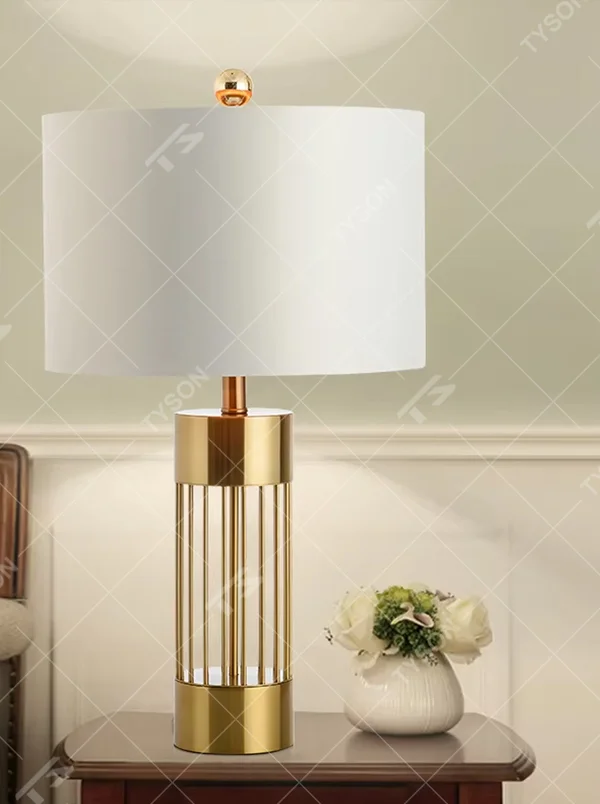 This light luxury table lamp features a gold metal hollow vertical strip column base, paired with a white fabric cylindrical lampshade and a top gold spherical decoration, with a simple and elegant shape, serving both lighting and decorative purposes, ideal for bedroom bedside tables, living room side tables, light luxury homestays and other spaces.