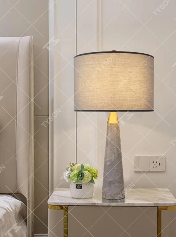 Light luxury marble cone table lamp, with a grey natural marble base, gold metal connection, off-white fabric lampshade with black trim, providing soft and warm light, designed to enhance the delicate texture of spaces, suitable for bedroom nightstands, living room side tables, modern light luxury homes and hotel guest rooms, etc.