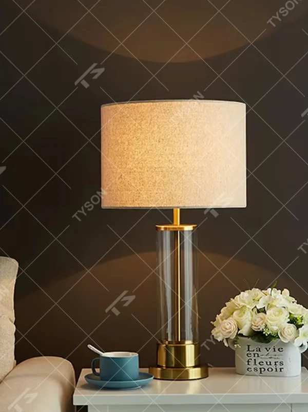 This modern light luxury table lamp features a transparent glass lamp body, paired with gold metal connectors and base, and an off-white fabric cylindrical lampshade that transmits light softly. It serves both lighting and decorative purposes, ideal for light luxury spaces such as bedroom bedside tables, living room side tables, and hotel guest rooms.