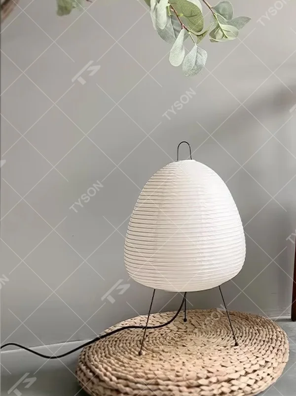 This wabi-sabi style egg-shaped table lamp features a striped light-transmitting paper lampshade, supported by a black metal tripod, with a simple and soft shape, serving both lighting and decorative purposes, ideal for bedroom bedside tables, homestay rooms, wabi-sabi style spaces and other scenarios.