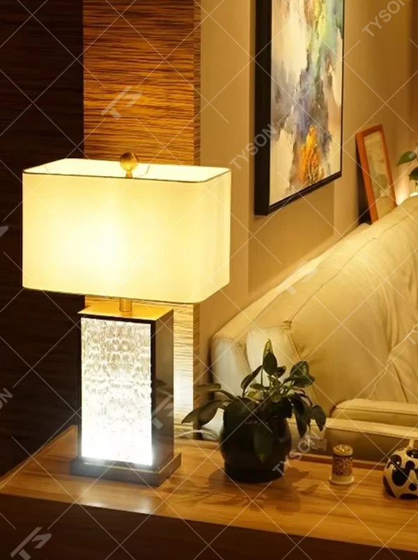 This modern light luxury table lamp features a gold metal frame, paired with a water-textured transparent glass lamp body and a white fabric rectangular lampshade. It serves both lighting and decorative purposes, ideal for light luxury spaces such as bedroom bedside tables, living room side tables, and hotel guest rooms.