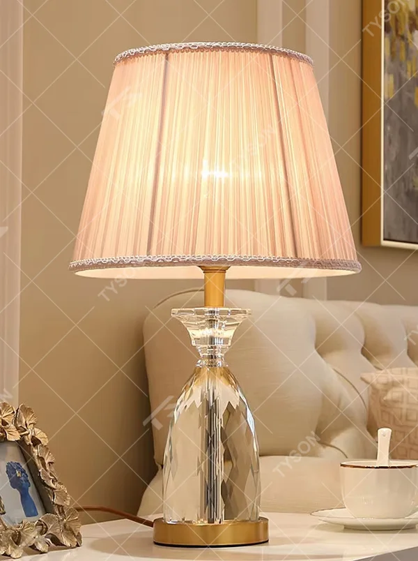 Light luxury crystal table lamp, with a diamond-cut crystal base, pink pleated fabric lampshade and gold metal details, providing soft and warm light, designed to enhance the elegant atmosphere of spaces, suitable for bedroom nightstands, living room side tables, princess rooms, etc.
