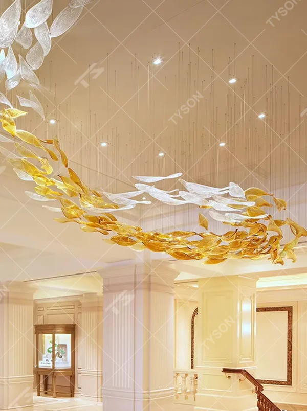 This large custom art glass chandelier features a streamlined school-of-fish/cloud-belt shape made of yellow-white gradient glass leaves, suspended in a floating manner, serving both lighting and artistic decoration purposes, ideal for high-ceiling commercial spaces such as sales offices, hotel lobbies, and high-end clubs.