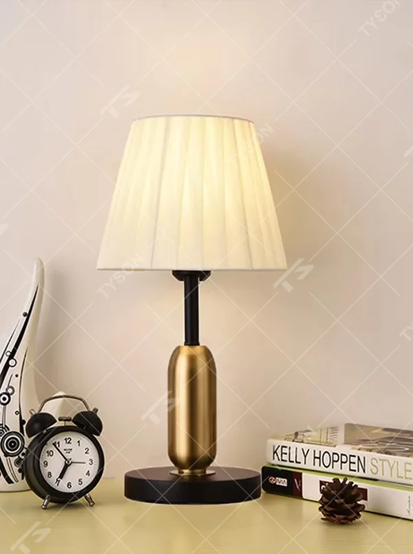 This is a light luxury minimalist style table lamp, featuring a gold metal lamp body paired with an off-white fabric lampshade. The black and gold color scheme offers a high-end texture, emitting soft and uniform light, serving both lighting and decorative purposes, suitable for bedroom nightstands, hotel guest rooms, light luxury living room side tables and other scenarios.